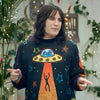 Person wearing a sweater with a UFO design in an indoor setting with plants and lights.